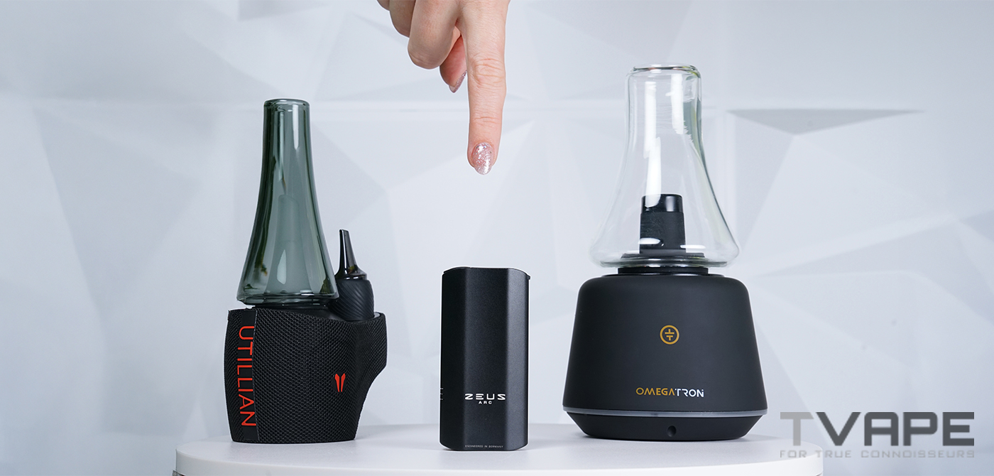 Trois vaporisateurs dispos&eacute;s sur une table&nbsp;: un Utillian avec un embout en verre &agrave; gauche, un Zeus Arc au centre et un Omegatron &agrave; droite. Une main au-dessus pointe vers celui du milieu.