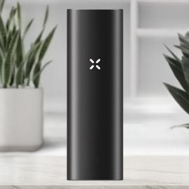 Vue avant du vaporisateur New PAX Mini en couleur Onyx, avec le logo PAX illuminé sur un corps en aluminium noir élégant, placé dans un intérieur moderne.